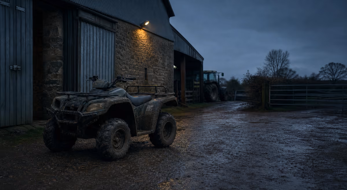 Muddy quad bike parked beside British farm buildings at dusk